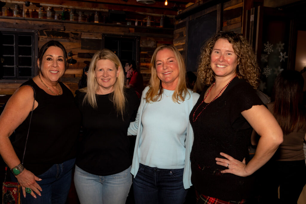 A group of women pose together in a rustic wood-paneled room decorated with snowflake window decals.