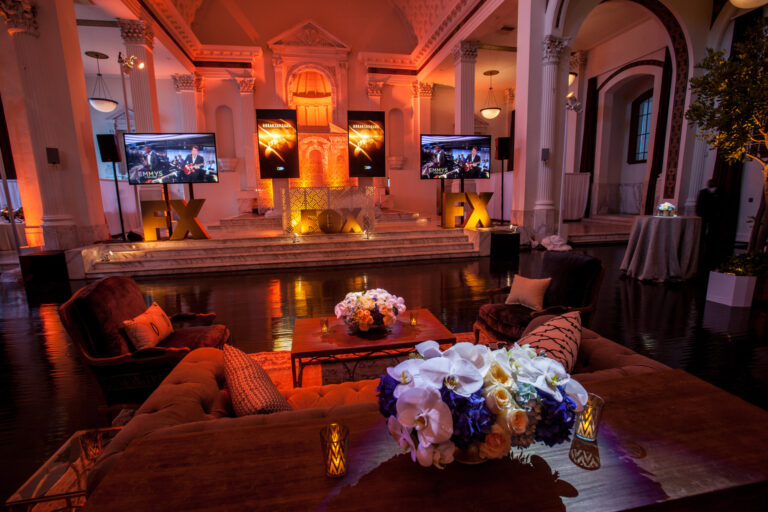 A warmly lit event lounge features a bar, cocktail tables, floral arrangements and wall-mounted screens.