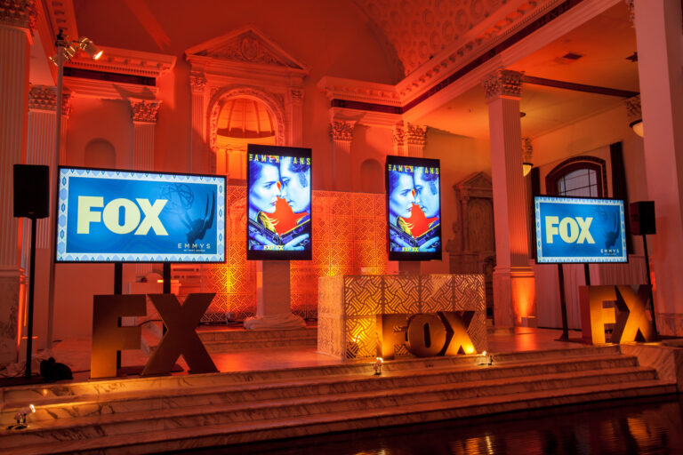 Two FOX-branded screens and large FX letters stand against an amber-lit event display wall.