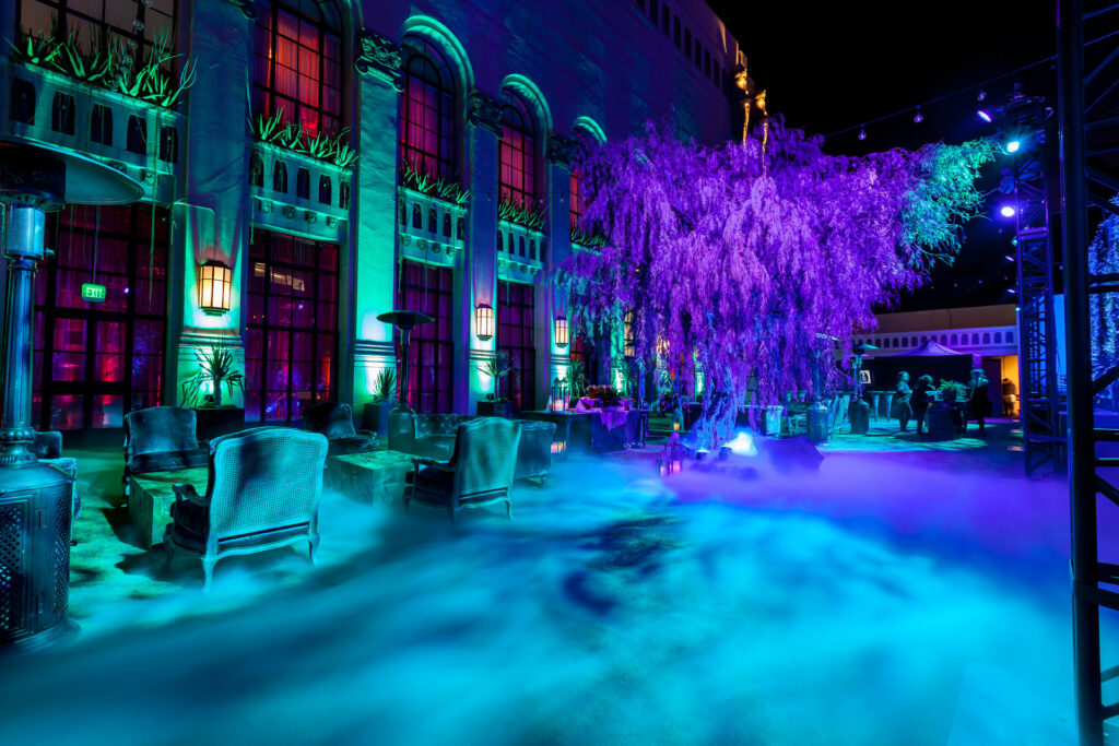 Blue-lit trees, a decorated table and lounge seating create a garden-like party setting.