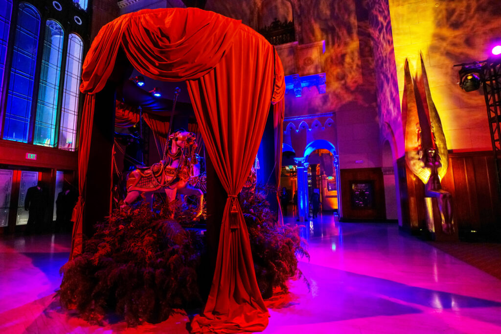 A carousel horse sits behind dramatic red curtains in a vividly lit event hall.