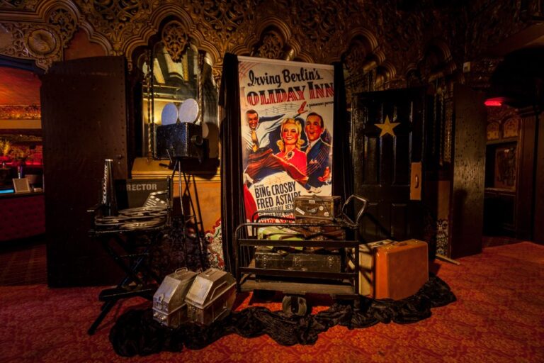 Irving Berlin's Holiday Inn themed entrance with vintage movie poster, stacked suitcases and a costumed bellhop greeting a guest, photographed in Los Angeles.