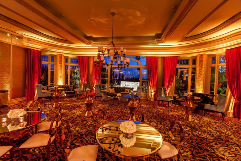 Premium hospitality lounge with red velvet drapery, gold chandelier and ornate ceiling with mirrored cocktail tables and floral arrangements, photographed in Los Angeles.