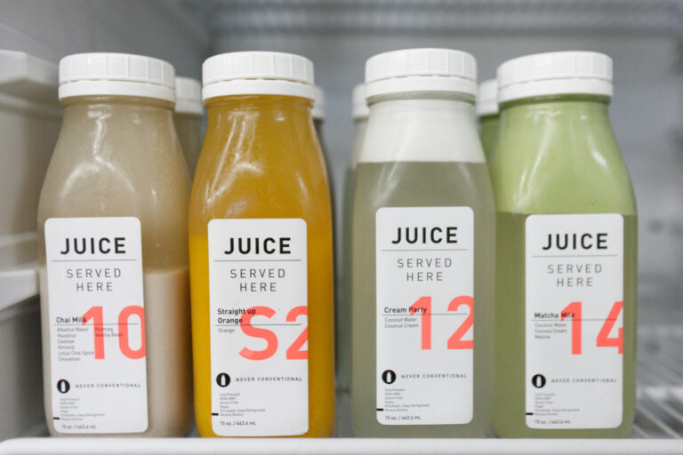 Four glass juice bottles with white caps and colorful labels arranged in a straight product lineup.