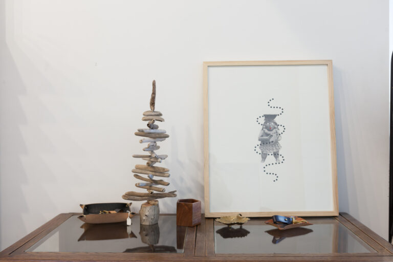 Sculptural stacked natural materials and framed line art displayed on a table against a white wall.
