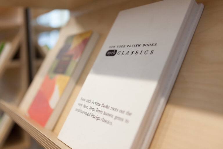 Open book titled The New York Times Best Sellers Classics displayed on a wooden shelf.