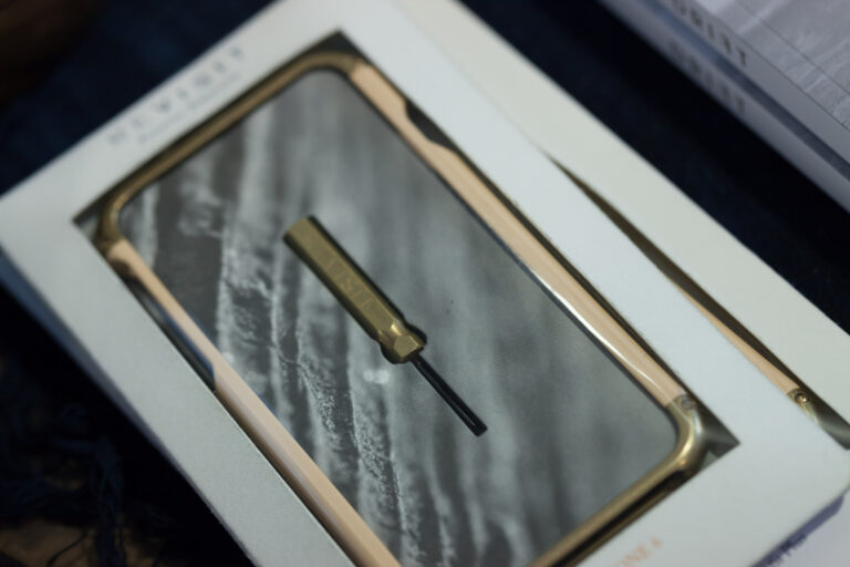 Framed botanical artwork and a small brass-colored object displayed on a dark tabletop.