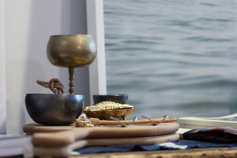 Small bowls and a metal goblet sit on a wooden tray beside a blue ocean view.