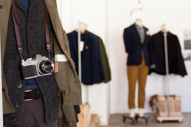 A camera hangs from a jacket displayed among clothing and mannequins in a bright retail showroom.