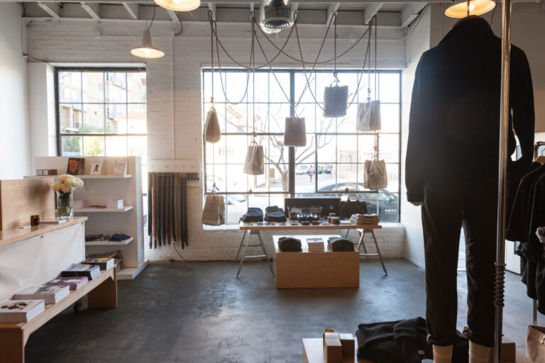 Wide view of an apparel boutique with mannequins, clothing racks, shelves and canvas bags suspended by the front windows.