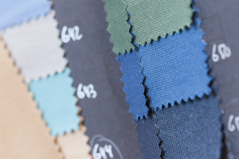 Blue, teal, green, gray and tan fabric swatches overlap on a dark board beside handwritten sample numbers.