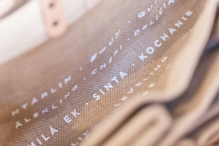 Close-up of tan woven canvas printed with white place names, including Santa Monica, against a blurred background.