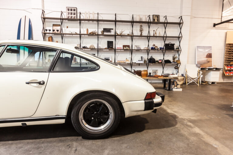 Close side view of a white classic sports car and dark rear wheel inside a showroom.