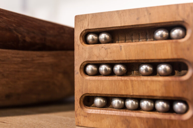 Rows of small metallic spheres sit in slots in a rectangular wooden display block.