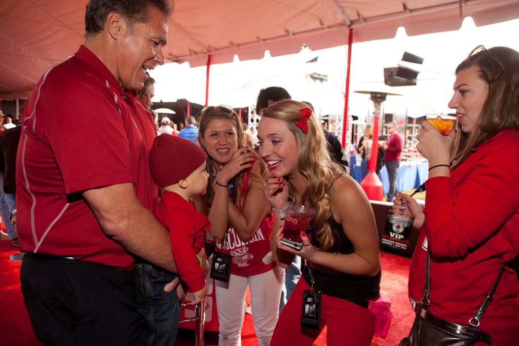 Guests enjoying ESPN’s Rose Bowl VIP hospitality event in Pasadena, California, with a man holding a young child as attendees smile and interact inside the branded hospitality tent.