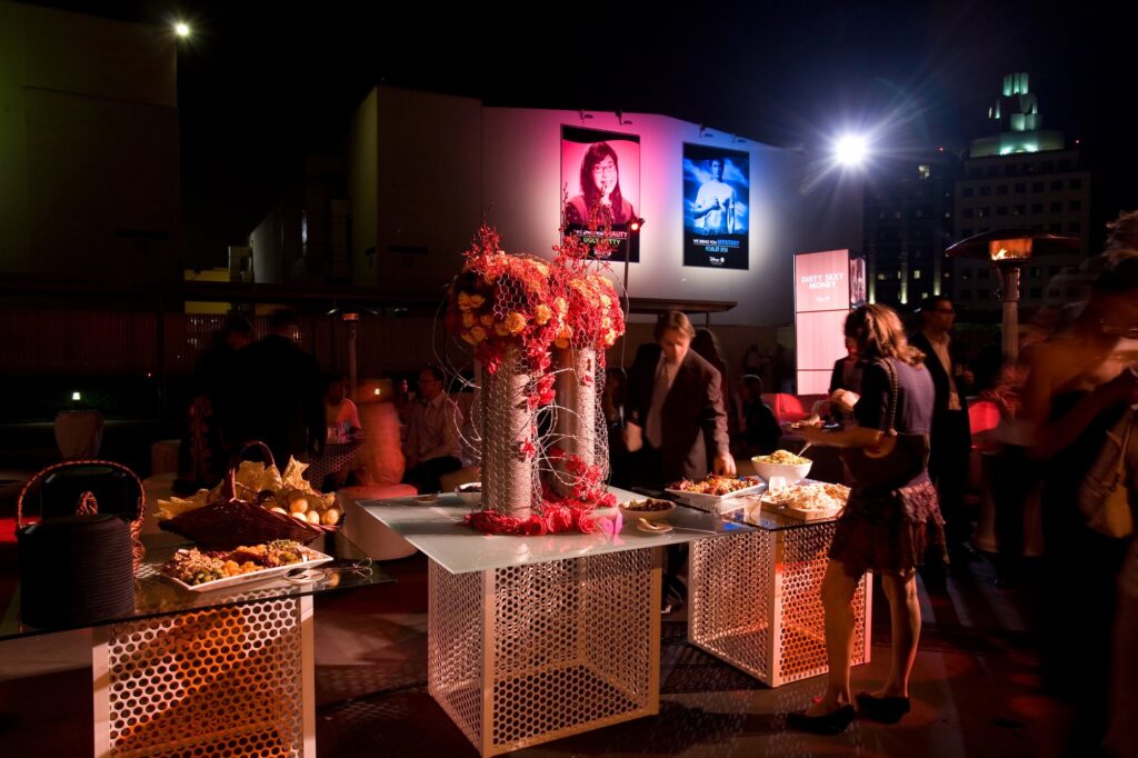 Tall red floral centerpiece beside guests in a warmly lit event lounge.