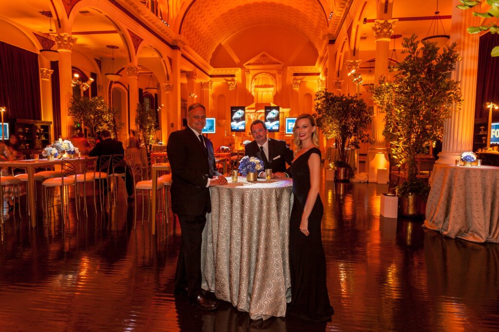 Guests gathered around cocktail tables in an amber-lit ornate ballroom.