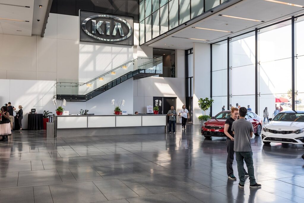 Attendees and display vehicles in a glass-walled Kia showroom.